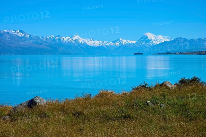 View over grassy shores to mountains across the lake, Lake Pukaki Viewpoint, Pukaki, Canterbury, South Island, New Zealand