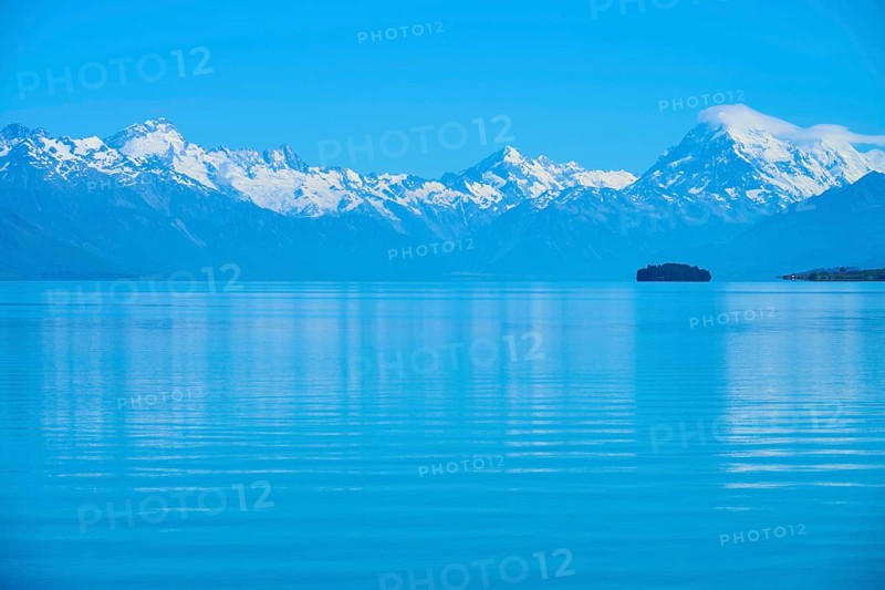 Expansive view of a tranquil lake with snow-capped mountains Mount Cook and an island, Lake Pukaki Viewpoint, Pukaki, Canterbury, South Island, New Zealand