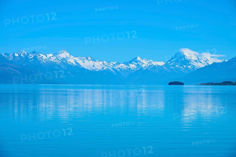 Mount Cook snow-capped mountains are reflected in a calm, blue lake, Lake Pukaki Viewpoint, Pukaki, Canterbury, South Island, New Zealand