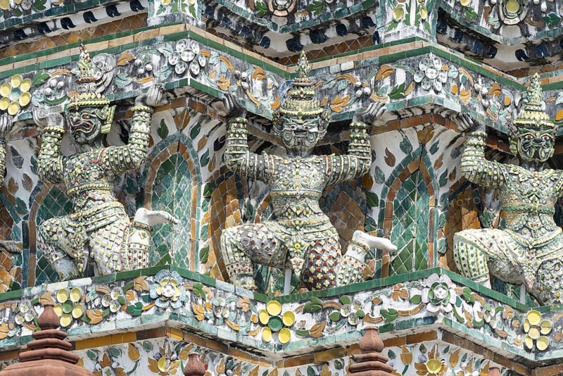 Demon figures (yaksha) supporting the central prang of Wat Arun decorated with colorful ceramic and porcelain ornaments, Thonburi, Bangkok, Thailand