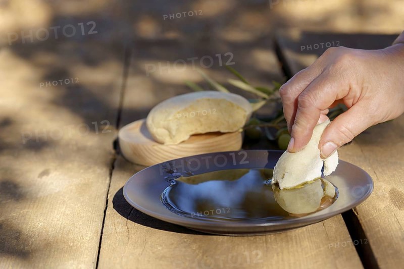 Hand dipping fresh homemade bread into healthy extra virgin olive oil, a staple of homemade mediterranean diet and cuisine