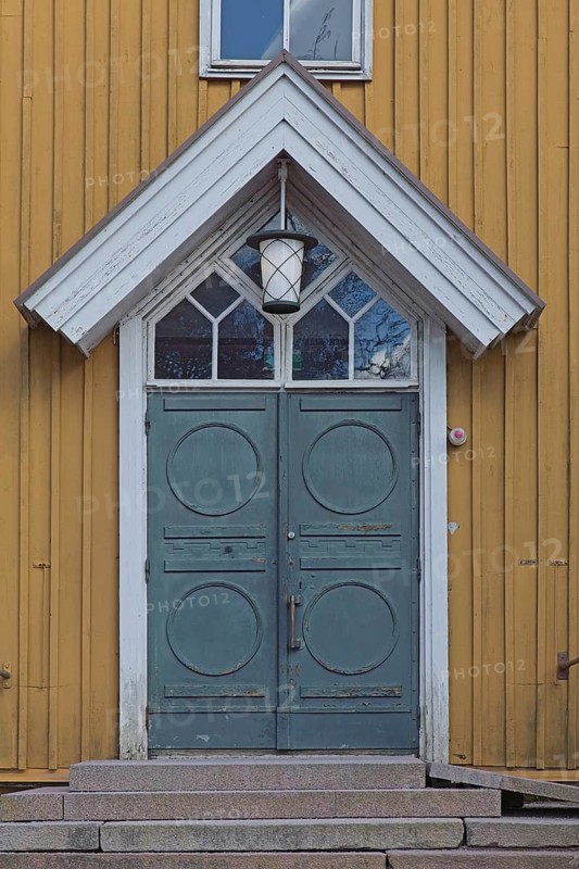 Closed old decorative double doors with white frame and window on top on a yellow board wall, Finland