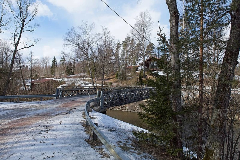 Gravel road on metal bridge over river Mustionjoki in winter, Junkarsborg, Finland