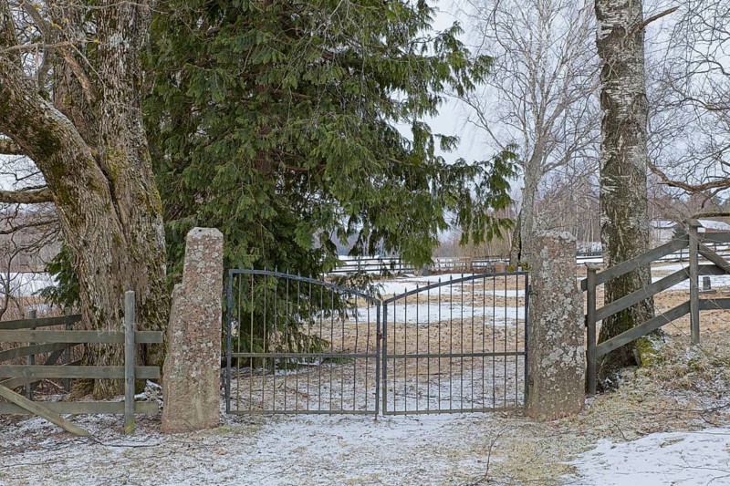 Closed old wrought iron gates mounted on stone gateposts to cemetery in winter, Degerby, Finland