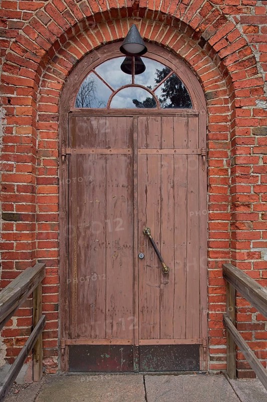 Closed old brown double doors with arch window on top on a red brick wall, Karjalohja, Finland