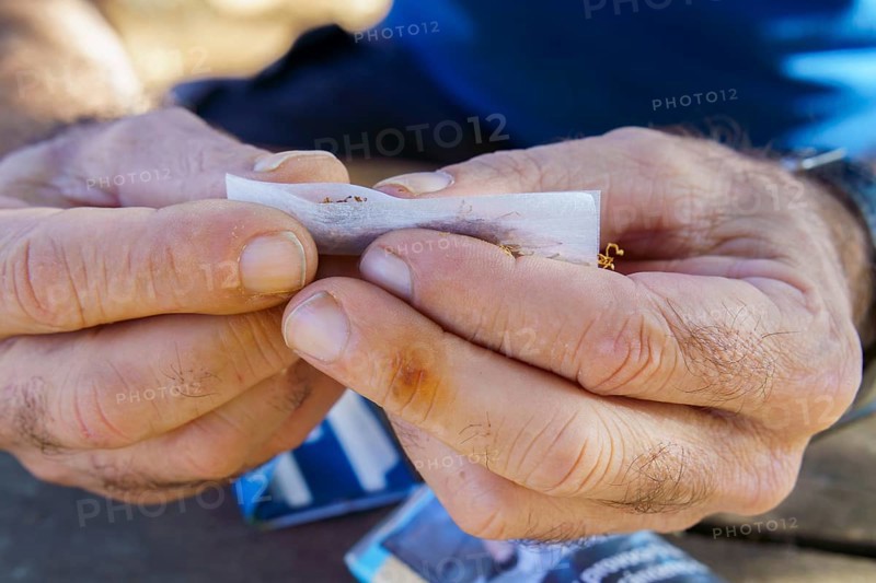 Close-up of hands with yellow stained fingers rolling tobacco into a cigarette, showing a smoking habit