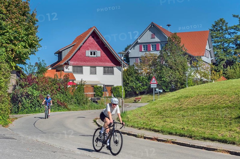 Country road with S-curve and two cyclists in Maria-Thann, Allgäu, Swabia, Bavaria, Germany