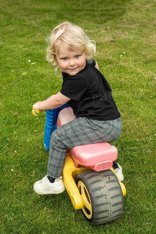 Blond Nordic girl, 3 years old, on a toy vehicle and looking back smiling in Ystad Municipality, Skåne County, Sweden, Scandinavia