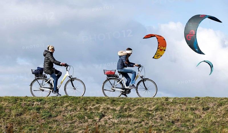 Cyclists ride across a dike and look at the sails of kite surfers, Fehmarn, 16.10.2025, Fehmarn, Schleswig-Holstein, Germany