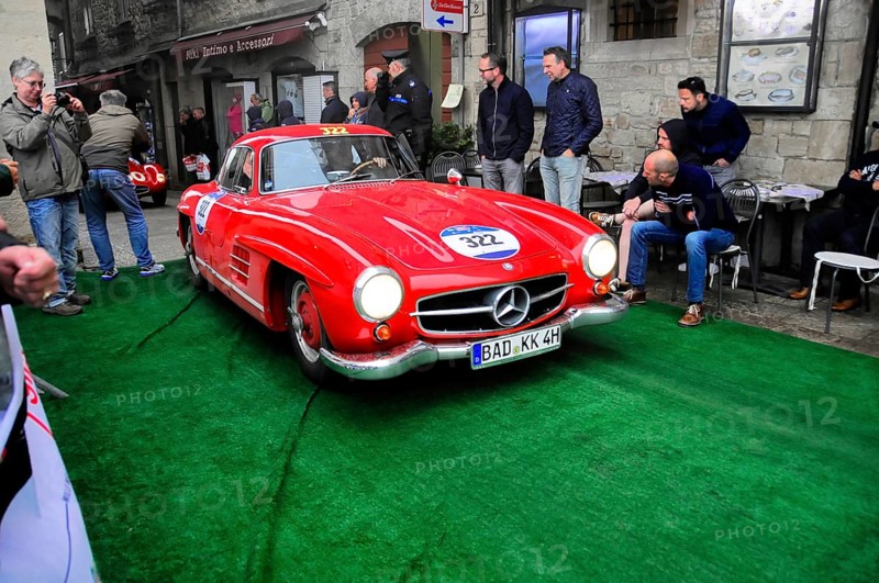 Roter 300 SL rolls across the green carpet through the old town, shiny chrome and rally number, lined with spectators, Mille Miglia 2016, time control, checkpoint, SAN MARINO, classic car racing. San Marino, Italia