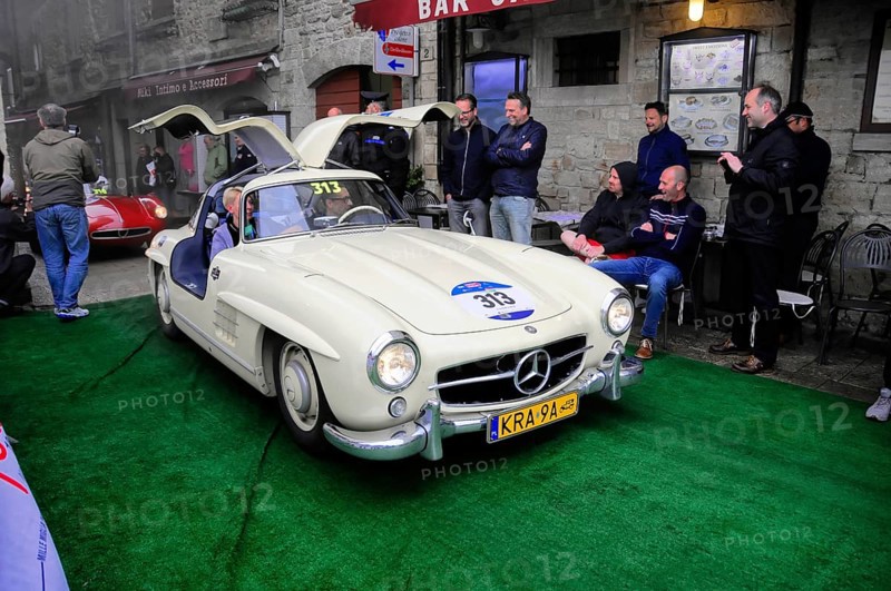 Creamy white 300 SL with open double doors poses on the green carpet, surrounded by smiling spectators in the old town, Mille Miglia 2016, time control, checkpoint, SAN MARINO, classic car racing. San Marino, Italia