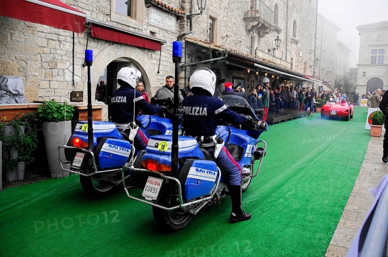 Police motorcycles escort a classic car rally through the stone old town, audience lines the green carpet, Mille Miglia 2016, time control, checkpoint, SAN MARINO, classic car racing. San Marino, Italia