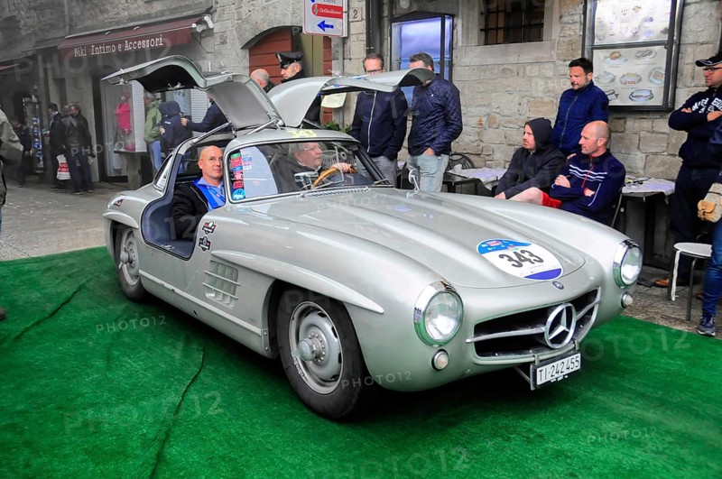 Silver 300 SL with open wing doors presents itself on the green carpet, interested audience in the old town, Mille Miglia 2016, time control, checkpoint, SAN MARINO, classic car racing. San Marino, Italia