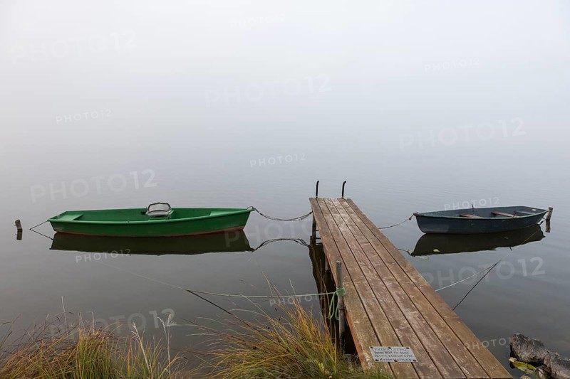 Two boats next to a wooden pier in a foggy, quiet autumn landscape, Hopfensee, Ostallgäu, Bavaria, Germany
