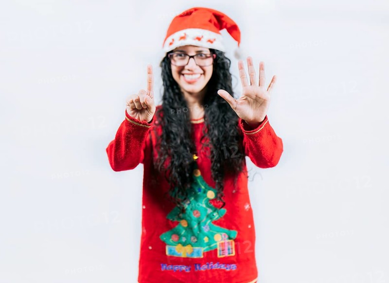 Happy girl in Christmas hat counting number SIX, isolated. Smiling girl in Christmas sweater counting number 6
