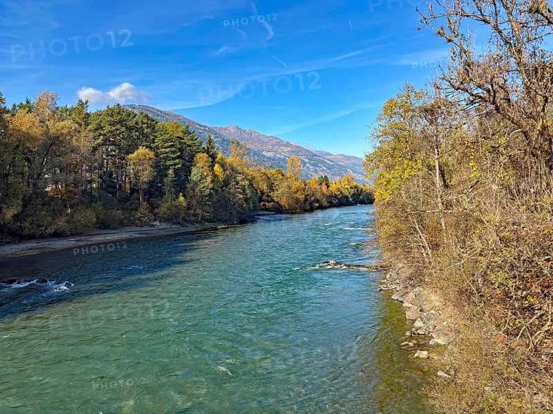 A quiet river surrounded by autumn trees and mountains under clear blue skies, Drau, Drauradweg, Lienz, Tyrol, Austria