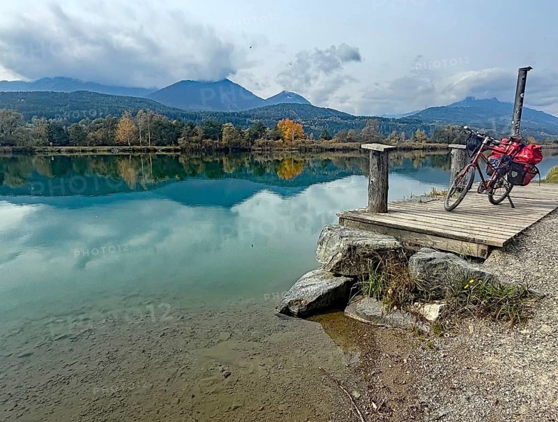 An idyllic lake with a bicycle on a jetty, surrounded by autumnal landscape and mountains, Drau, Villach, Drau cycle path, Carinthia, Austria