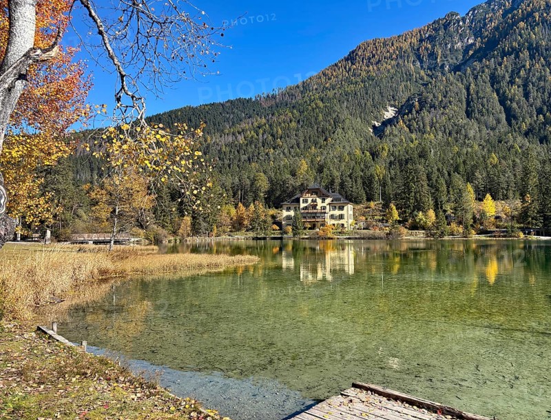 A lakeside villa surrounded by autumnal forests and clear reflection in the water, Lake Toblach, Lake Dobbiaco, South Tyrol, Italy