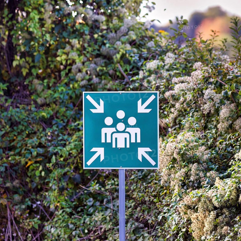 Green outdoor sign, pictogram showing group of people surrounded by four arrows, escape sign for assembly point, meeting point, in case of fire, evacuation, escape route, North Rhine-Westphalia, Germany