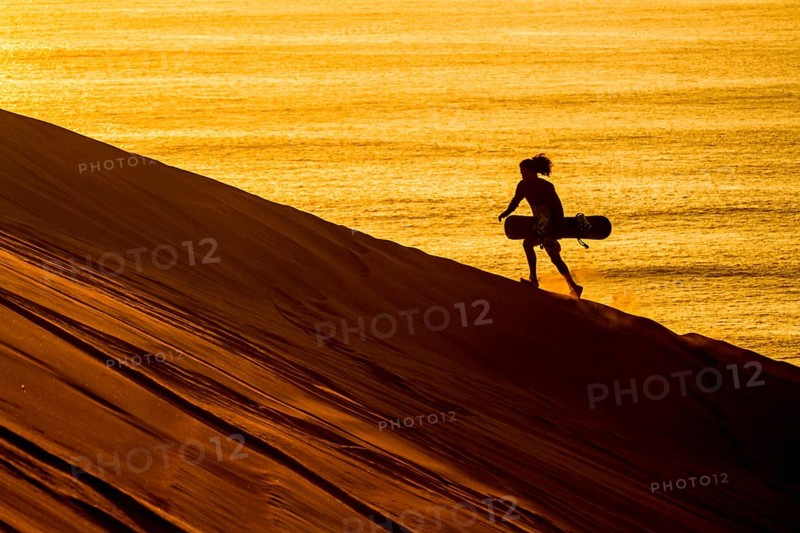 Silhouette of a sandboarder walking at sunset in Cerro Dragon, a sand dune located next to the city of Iquique, in Atacama Desert. Iquique, Tarapaca Region, Chile. 15.11.15