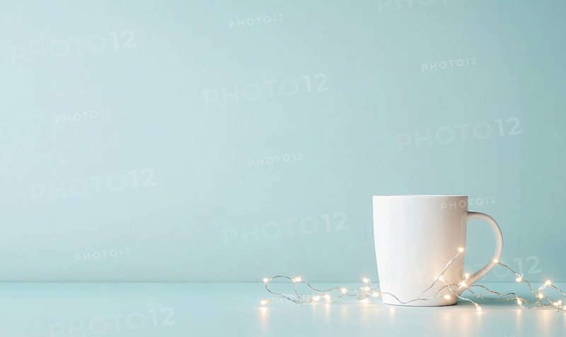 A white coffee cup sits on a table next to a string of lights. The scene is simple and calming, with the white cup and lights creating a sense of warmth and comfort. AI generated