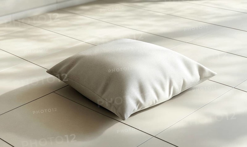 A white pillow sits on a tile floor. The pillow is small and square in shape. The floor is white and the pillow is the only object in the image. AI generated