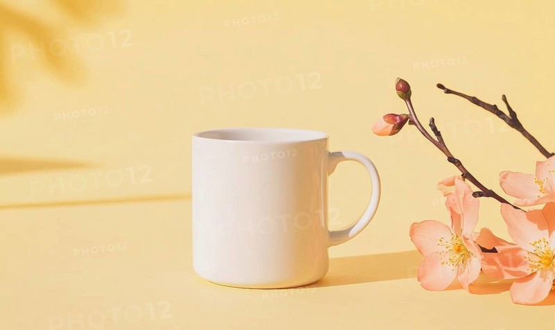 A white coffee cup sits on a yellow background with pink flowers in the foreground. The cup is empty, and the flowers are in full bloom, creating a sense of freshness and vitality. AI generated