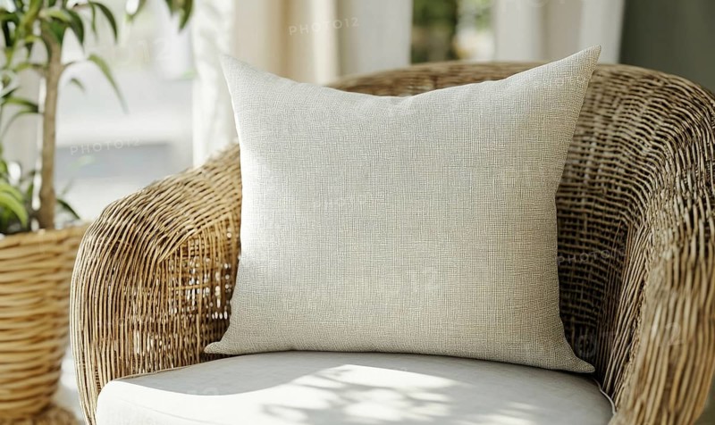 A white pillow sits on a wicker chair in front of a potted plant. The pillow is patterned with a checkered design and is placed on the chair in a way that it is visible from the front. AI generated