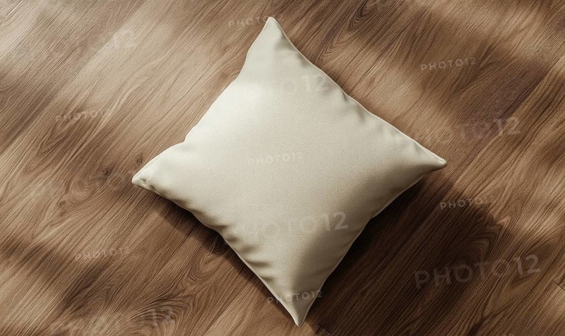 A cream pillow on a hardwood floor with natural light and shadows. AI generated
