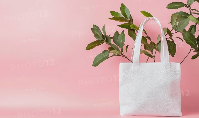 A white bag with a leaf on it is on a pink background. The bag is placed in front of a plant, which adds a touch of nature to the scene. The combination of the white bag. AI generated