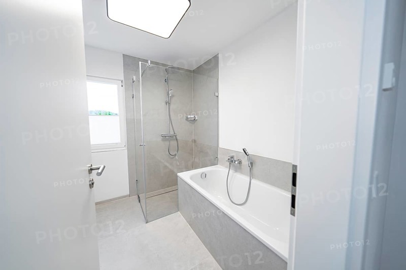 Modern bathroom with floor-level shower and tub in front of large format grey tiles and plenty of daylight, house renovation, energy renovation, Metzingen, Germany