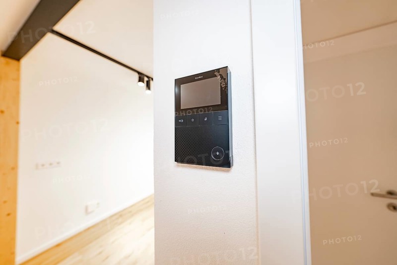 Wall intercom with display in a bright corridor next to a white door and warm parquet, house renovation, energy renovation, Metzingen, Germany