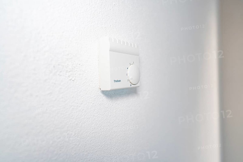 Close-up of a white room thermostat on a plastered wall in a bright, modern environment, house renovation, energy renovation, Metzingen, Germany
