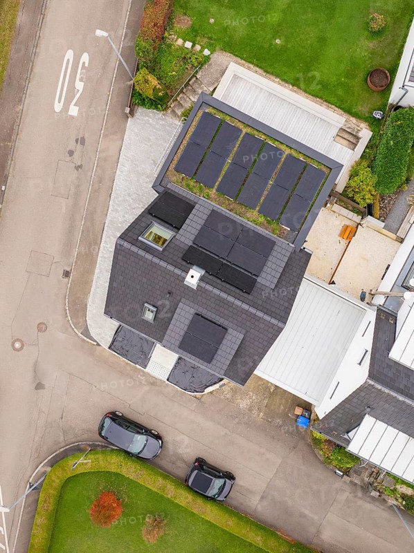 Top view of house with PV modules and carport green roof, two parked cars and curved road, house renovation, energy renovation, Metzingen, Germany
