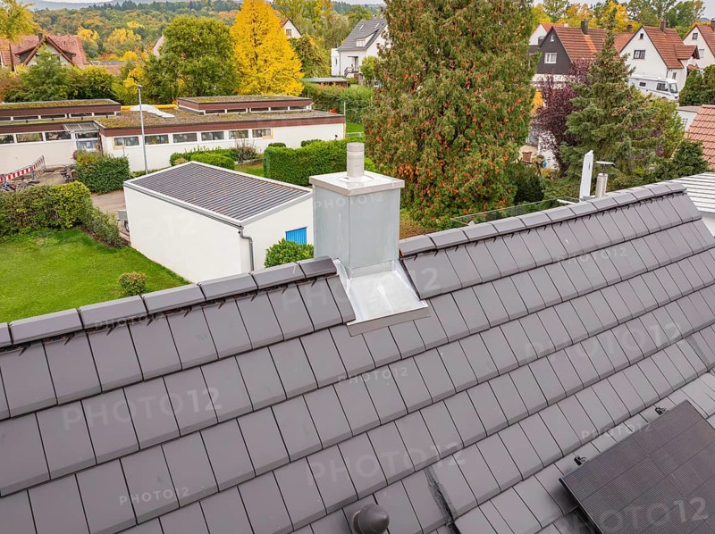 Roof with anthracite-colored tiles and modern chimney, behind it quiet residential area with autumn trees, house renovation, energy renovation, Metzingen, Germany
