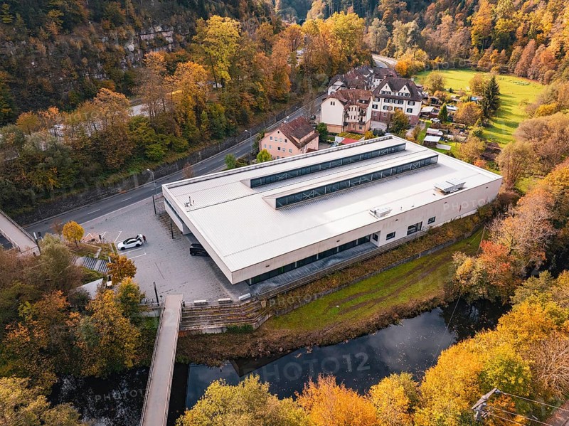 Sports hall nestled in an autumnal setting with a small river and bridge nearby, Walter Lindner Sporthalle Calw, Black Forest, Germany