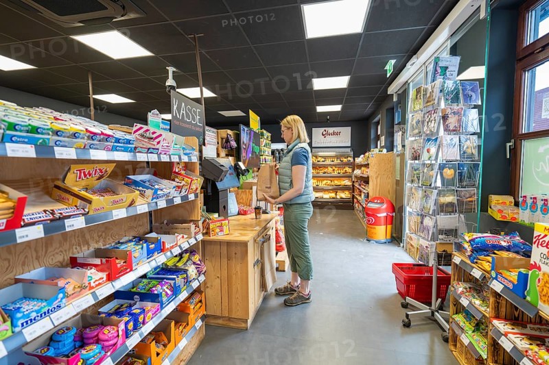 Customer stands at the cash register in a supermarket, surrounded by shelves with various snacks, 24-hour Aunt M Store