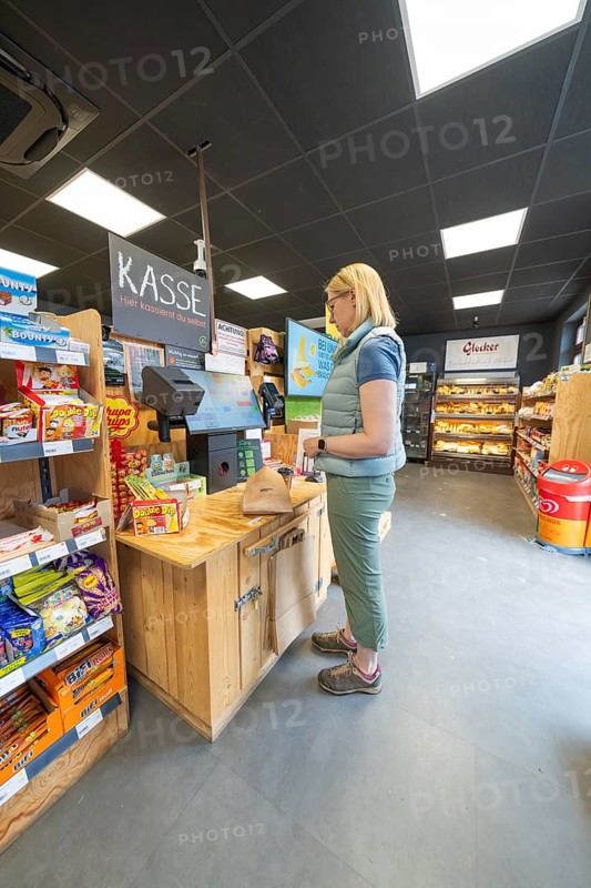 A woman stands at the cash register in a supermarket with snacks and products on the shelves, 24 hours Aunt M Store