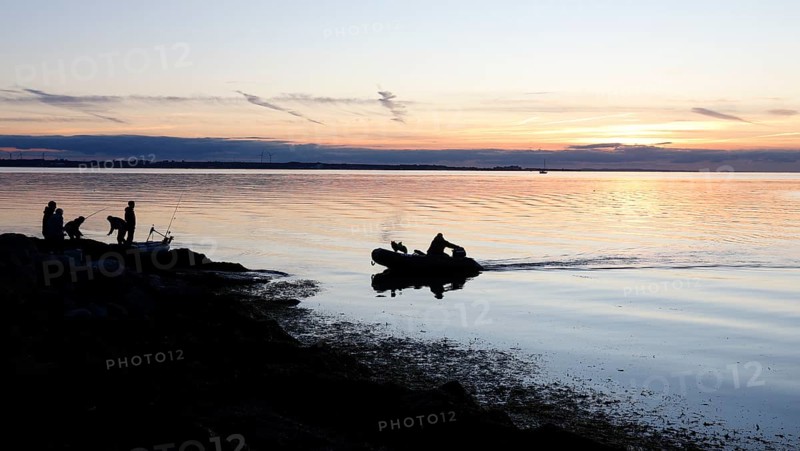 Angler on the beach during sunset, an angler docks on the shore with his inflatable boat and dog, Fehmarn island, 18.10.2025, Fehmarn, Schleswig-Holstein, Germany