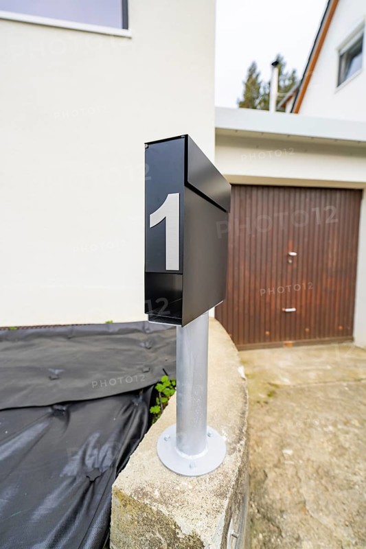 Close-up of a modern black mailbox in front of garage and plaster façade, house renovation, climate renovation, Metzingen, Germany