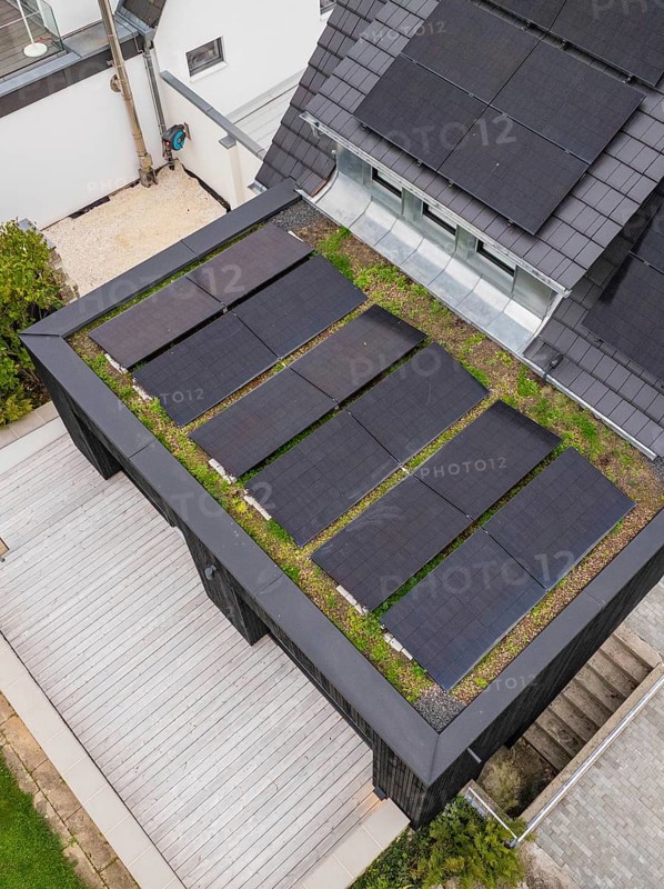 Detailed view of a green flat roof with raised black solar panels next to a bright wooden terrace, house renovation, climate renovation, Metzingen, Germany