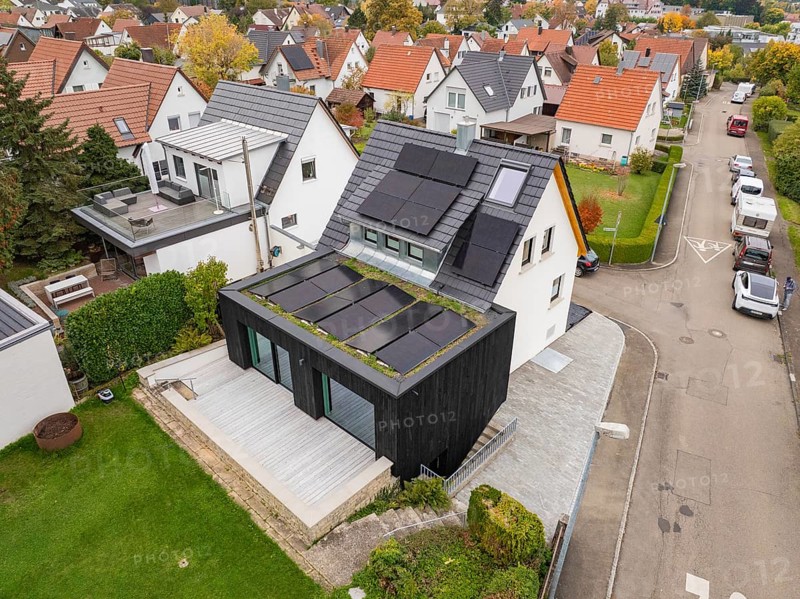 Angled aerial view of a modernized house with photovoltaic on gable roof and green extension in a well-maintained residential area, house renovation, climate renovation, Metzingen, Germany