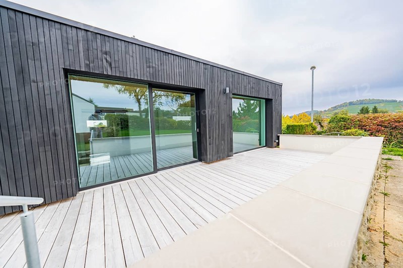 Large terrace with light wooden deck against black façade and sliding doors, wide views of autumn surroundings, house renovation, air-conditioning renovation, Metzingen, Germany