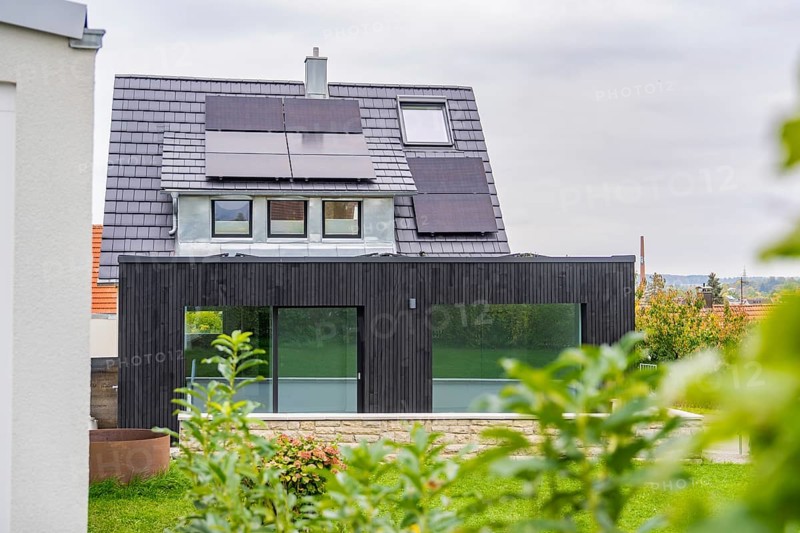 Modern house extension with glass front and solar panels, framed by plants in the foreground, quiet garden atmosphere in cloudy skies, house renovation, air conditioning renovation, Metzingen, Germany