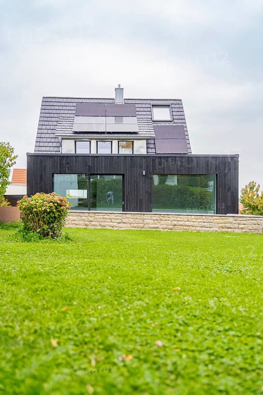 Single-family house with solar panels and black glass-fronted extension, large lawn in the foreground, quiet residential area with overcast sky, house renovation, air-conditioning renovation, Metzingen, Germany