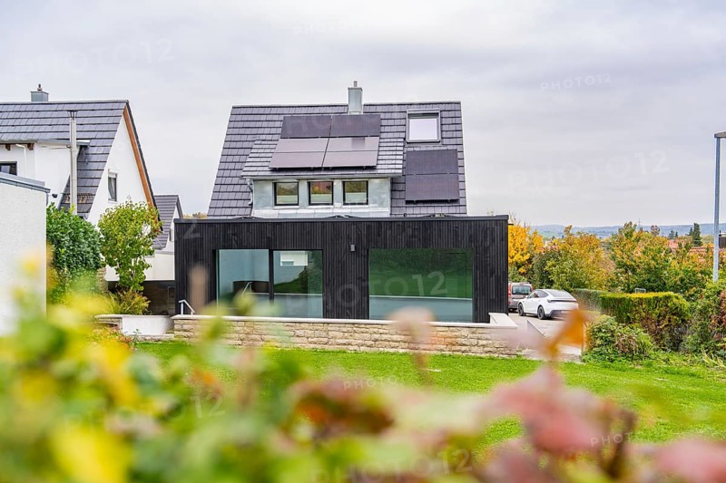 House with solar panels and black extension, view over garden to quiet street with parked car, house renovation, air conditioning renovation, Metzingen, Germany