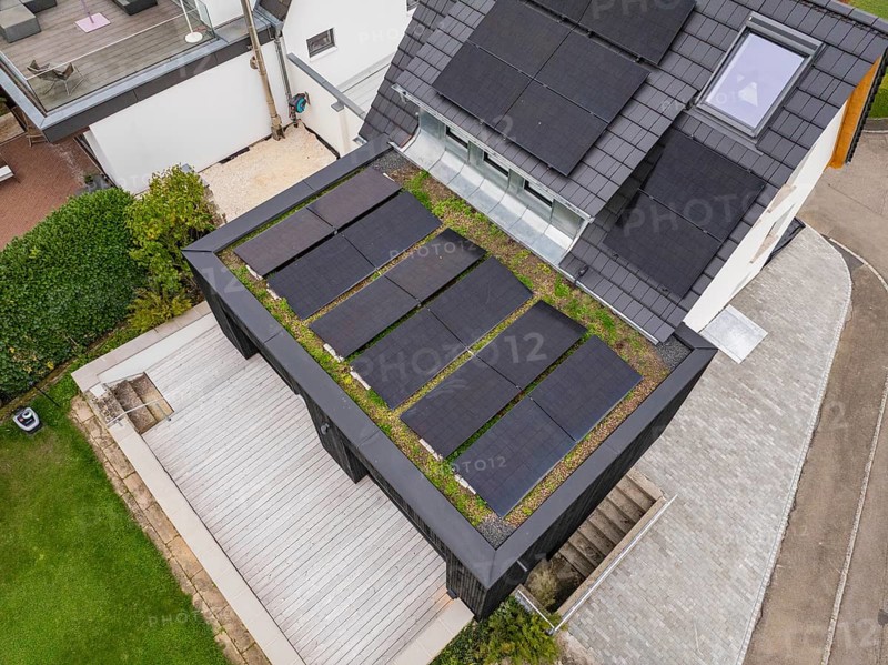 Diagonal view of the green extension with solar panels, adjacent wooden deck area and paved driveway, house renovation, climate renovation, Metzingen, Germany