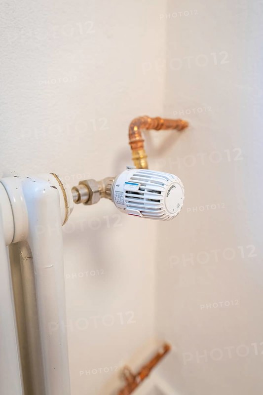 Detail of a radiator thermostat with copper lines on a white wall, house renovation, climate renovation, Metzingen, Germany