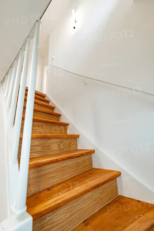 Wooden staircase with white railing and wall lamp in bright, simple staircase, house renovation, climate renovation, Metzingen, Germany