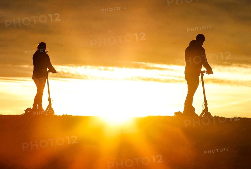 E-scooter drivers ride across a dike on the island of Fehmarn at sunset, 13.10.2025, Fehmarn, Schleswig-Holstein, Germany